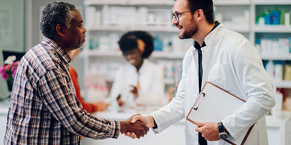 Male pharmacist shaking hands with a senior african american man patient in pharmacy stock photo